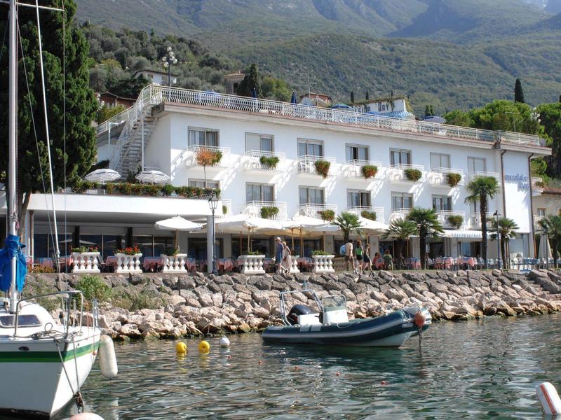 Hotel sul lungolago con terrazza, barche e vista sulle montagne sullo sfondo.