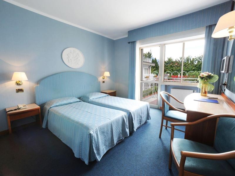 Camera d'hotel moderna con due letti, tonalità di blu e vista su un balcone.