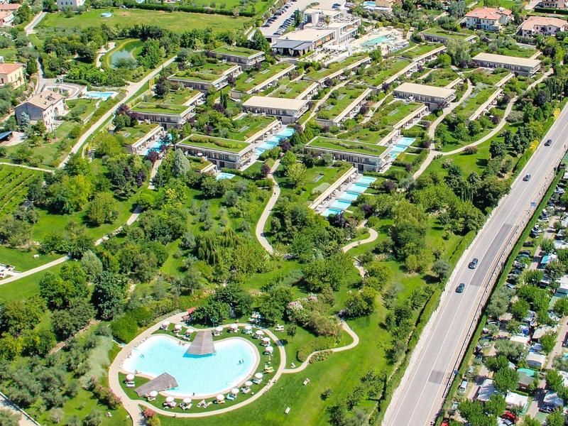 Aerial view of a hotel with multiple pools, green gardens, and an adjacent road.