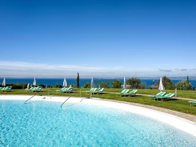 Round swimming pool with lounge chairs and umbrellas, ocean view.