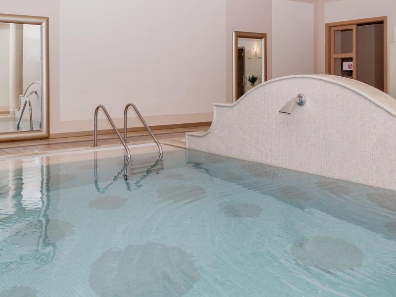 Indoor pool with clear blue water and metal ladder in a quiet hotel room.