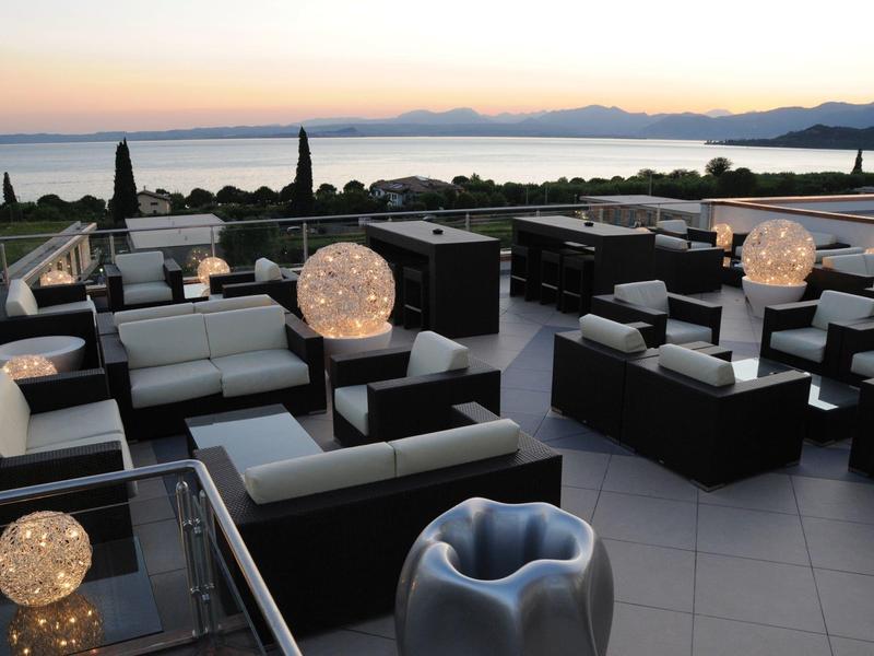 Modern terrace with seating areas and illuminated spheres overlooking the sea at sunset.