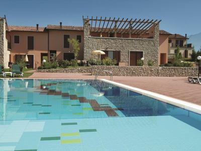 Modern pool in front of holiday homes with stone and plaster façades under blue sky.