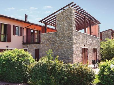 House with stone wall and pergola surrounded by green bushes under a blue sky.