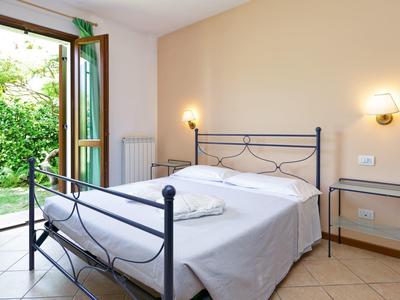 Bright bedroom with metal bed, open window overlooking green garden.