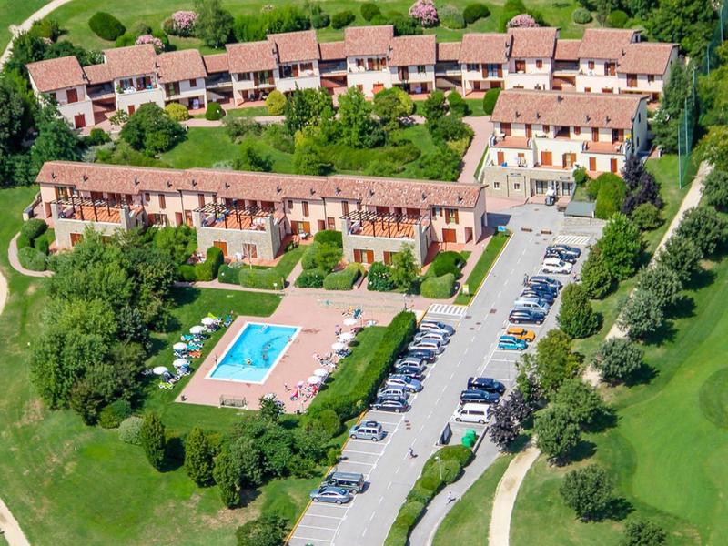 Aerial view of a hotel with pool, parking, and golf course in a green setting.