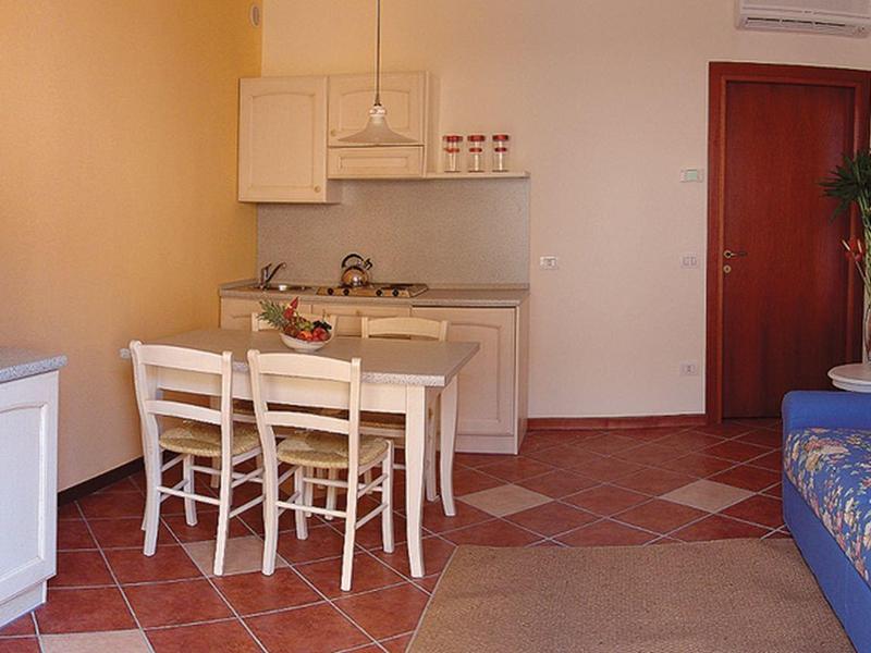 Living room with dining table, sofa, TV, and open kitchenette in warm tones.