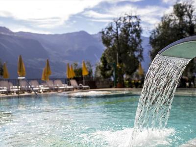 Piscine avec cascade et chaises longues devant un paysage montagneux par une journée ensoleillée