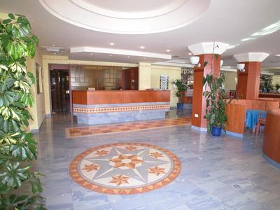 Hol hotelowy z recepcją, marmurową podłogą i dużymi roślinami.