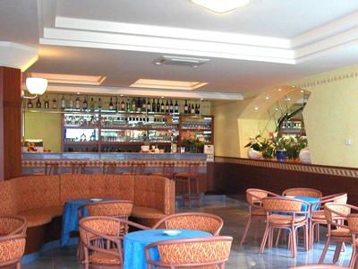 Bar z długim ladą, półkami pełnymi butelek i miejscami do siedzenia z stolikami.