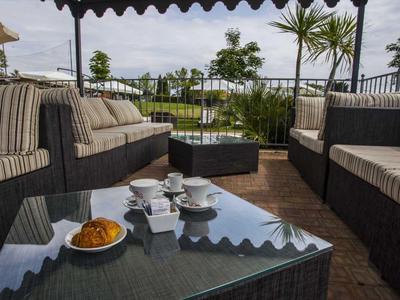 Terrasse mit Sitzgruppe aus Rattan, gestreiften Polstern, Kaffee und Croissant auf Glas-Tisch.