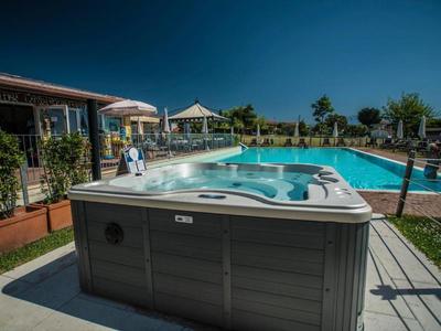 Ein großer grauer Whirlpool steht vor einem blauen Schwimmbecken unter klarem Himmel.