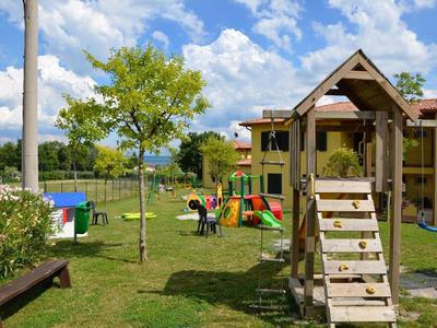 Kinderspielplatz mit Klettergerüst, Rutsche, bunten Spielhäusern und Bäumen auf grünem Rasen.