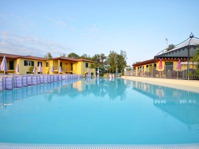 Großer, klarer Pool mit blauer Wasseroberfläche, umgeben von gelben Gebäude und Bäumen im Hintergrund.