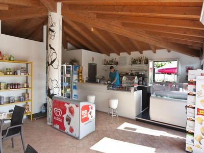 Innenraum einer Eisdiele mit Holzdecke, Kühlschränken, Theke, Stühlen und Regalen mit Produkten.