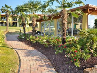 Gepflasterter Weg führt an Palmen und bunten Blumen am Gebäude im sonnigen Garten vorbei.