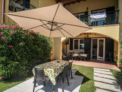 Garten mit grünem Rasen, Tisch mit Blumen-Tischdecke, Stühlen und großem Sonnenschirm vor Terrasse.
