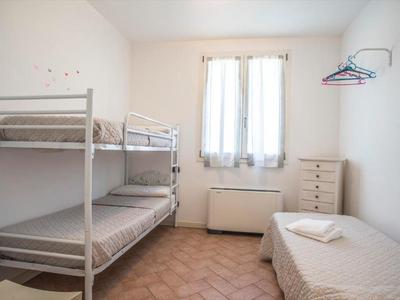 Kleines Schlafzimmer mit Etagenbett, Einzelbett, Kommode und Garderobenhaken an weißer Wand.