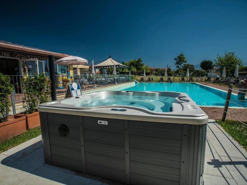Ein großer grauer Whirlpool steht vor einem blauen Schwimmbecken unter klarem Himmel.