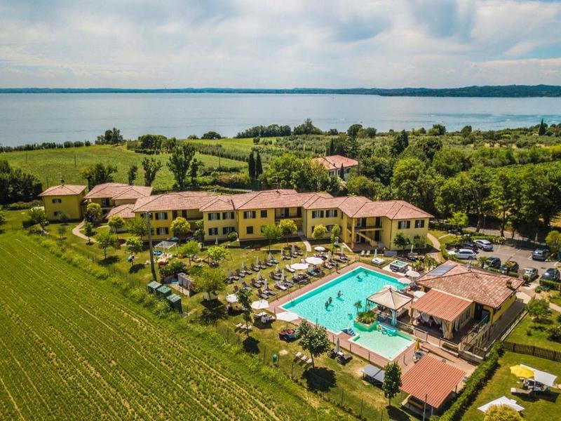 Große Ferienanlage mit Pool, grünen Wiesen und weitem See im Hintergrund unter leicht bewölktem Himmel.