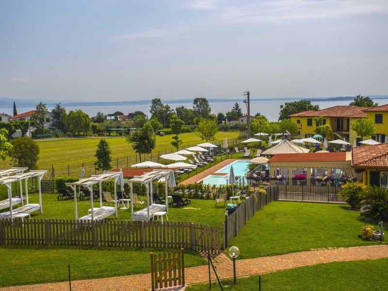 Luxusanlage mit Pool, grünen Rasenflächen, weißen Pavillons und gelben Gebäuden bei sonnigem Wetter.