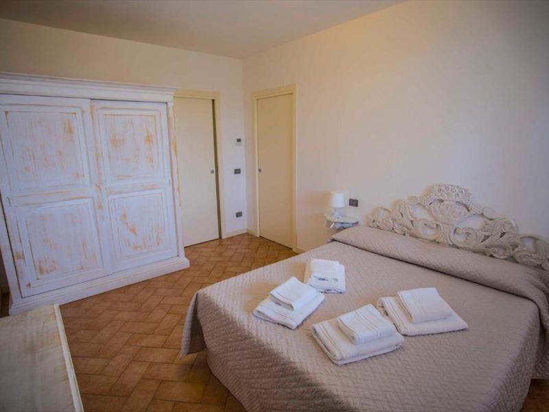 Einfaches Schlafzimmer mit großem, verziertem Doppelbett, kleinem Nachttisch und weißem Schrank.