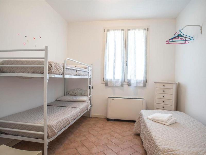 Kleines Schlafzimmer mit Etagenbett, Einzelbett, Kommode und Garderobenhaken an weißer Wand.