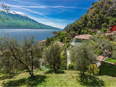 Landschaft mit See, grünen Bäumen, kleinen Häusern und Bergen unter blauem Himmel mit Wolken.