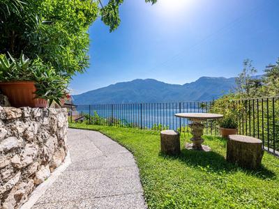 Gepflegter Gartenweg mit Sitzgelegenheiten und Blick auf See und Berge bei Sonnenschein.