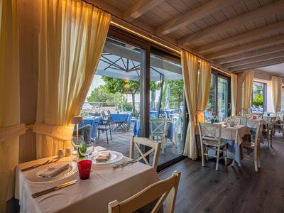 Gemütliches Restaurant mit weißen Tischen, Holzstühlen und großen Fenstern zum Außenbereich.