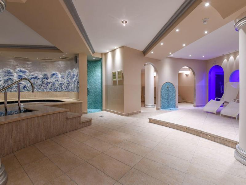 Modernes Wellnesszimmer mit weißen Säulen, beleuchteten Nischen und großen Fliesen am Boden.