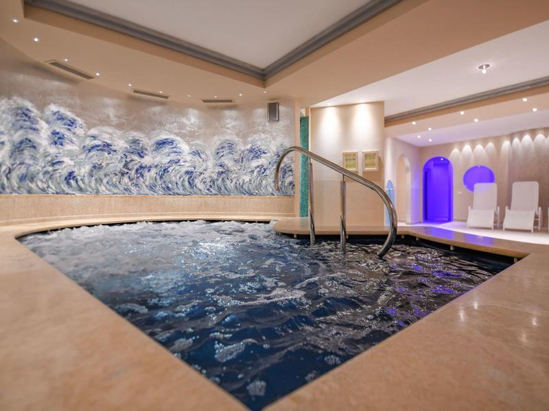 Moderner Innenpool mit Mosaikfliesen und blau-weißer Wellenwand in elegantem Wellnessbereich.