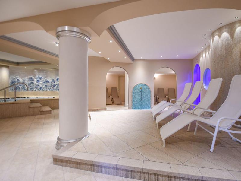 Moderner Wellnessbereich mit weißen Liegestühlen, Säulen und blauen Akzentlichtern an der Wand.