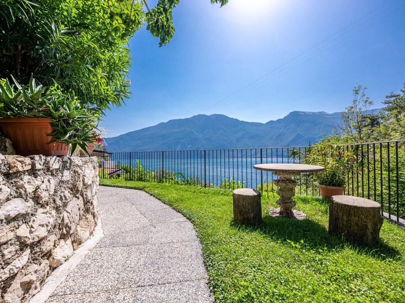 Gepflegter Gartenweg mit Sitzgelegenheiten und Blick auf See und Berge bei Sonnenschein.