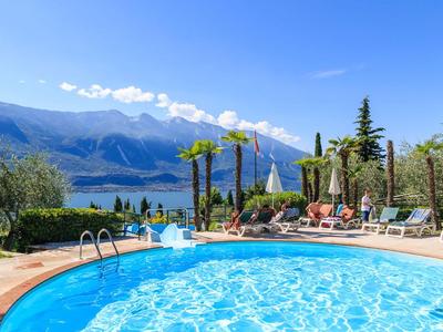 Piscina circolare dell'hotel con lettini e vista su montagne e lago sotto cielo sereno.
