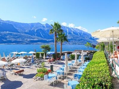 Hotel costiero con terrazza solarium, lettini e vista su montagne e lago.
