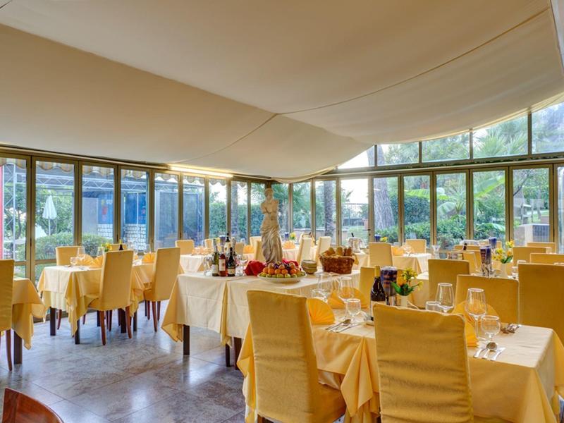 Ein helles Restaurant mit großen Fenstern, gelben Stühlen und sorgsam gedeckten Tischen.