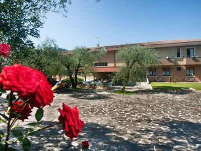 Rotes Rosenbouquet im Vordergrund, dahinter ein großer Hof mit Olivenbäumen und zweistöckigem Haus.