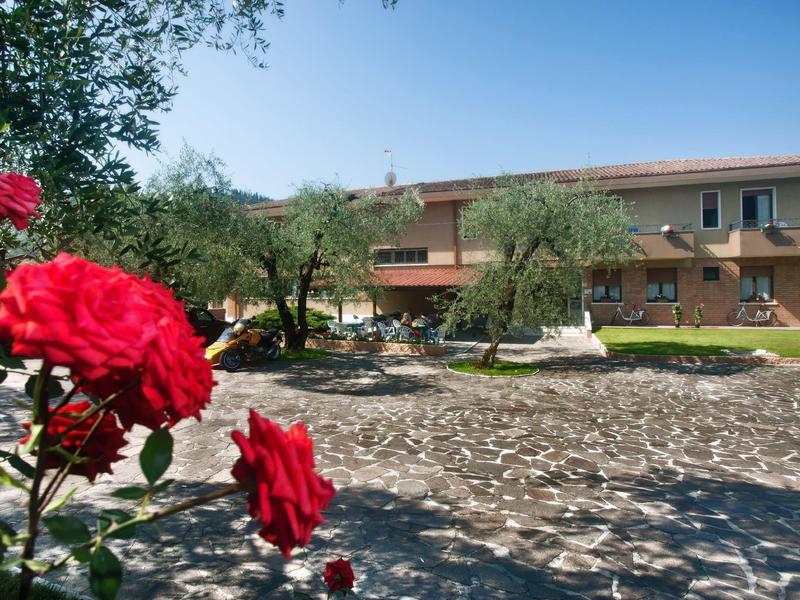 Rotes Rosenbouquet im Vordergrund, dahinter ein großer Hof mit Olivenbäumen und zweistöckigem Haus.