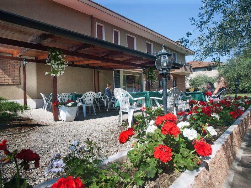 Terrassenbereich mit Tischen, Stühlen und roten Blumen im Vordergrund unter blauem Himmel.