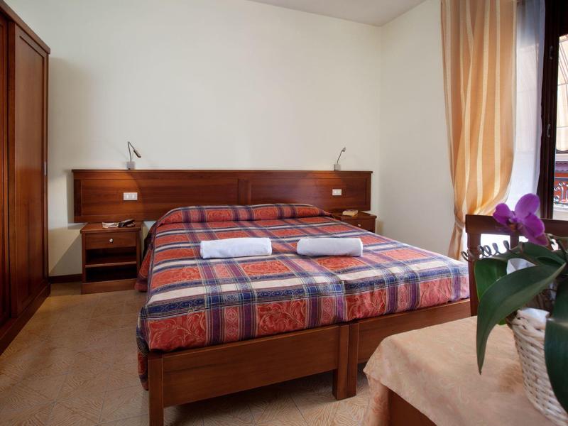 Schlichtes Schlafzimmer mit Holzmöbeln, kariertem Bettbezug und zwei Handtüchern auf dem Bett.