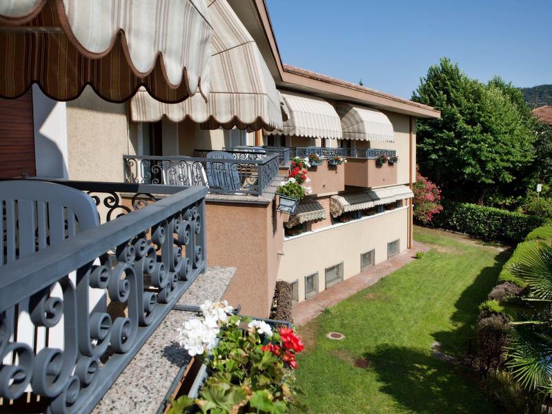 Haus mit Balkon, weißen Wänden und blumenverzierten Fensterbänken, grüner Garten im Vordergrund.