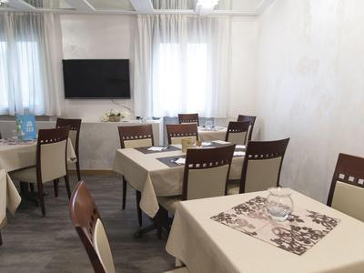 Comedor iluminado con mesas, sillas y un televisor en la pared.