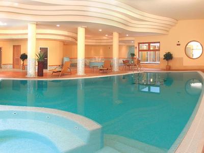 Indoor pool with hot tub in brightly lit wellness area with wave-shaped ceiling.