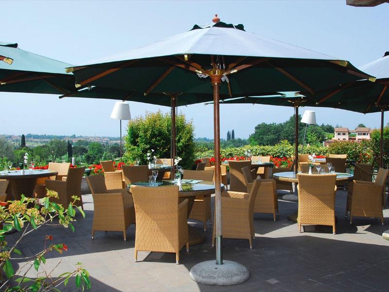 Terrace with seating, tables, and large umbrellas overlooking a green landscape.