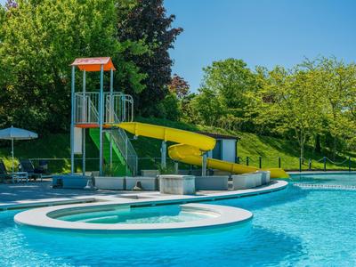 Piscina all'aperto con scivolo giallo e sedie a sdraio in un ambiente verde