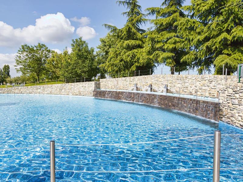Acqua blu chiara in una piscina moderna con muri di pietra naturale e alberi sullo sfondo.