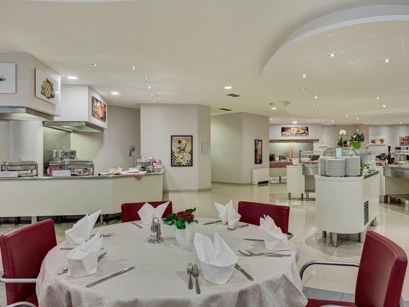 Ristorante elegante con tavoli rotondi apparecchiati e sedie rosse in una stanza luminosa.