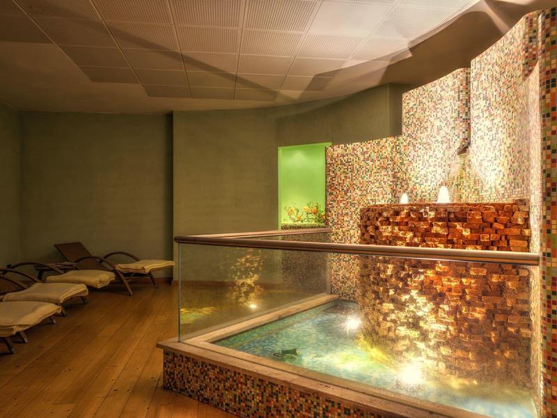 Vasca idromassaggio moderna con piastrelle a mosaico e lettini in un'area spa rilassante.