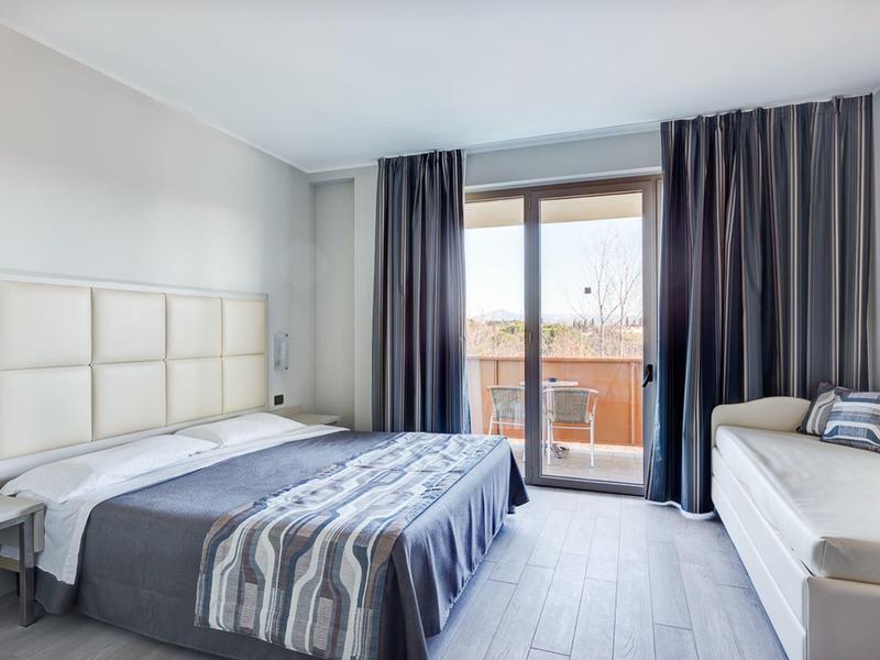 Camera d'hotel moderna con letto matrimoniale, biancheria grigia e accesso al balcone con vista.